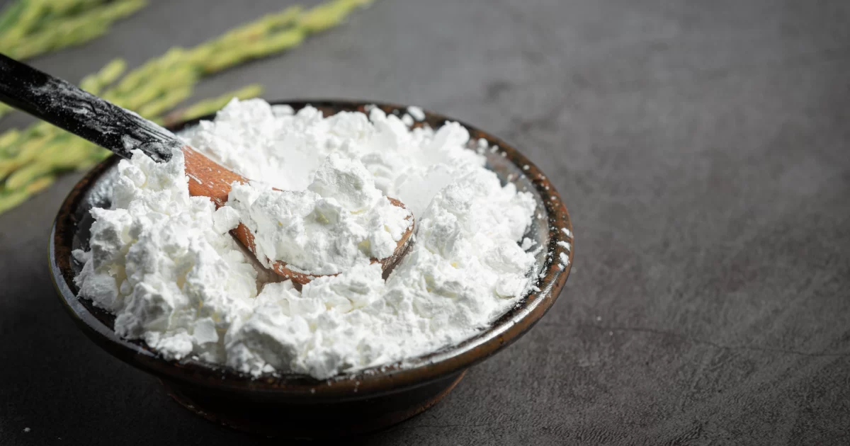 Fine calcined clay powder placed in a bowl with a wooden spoon on a dark surface