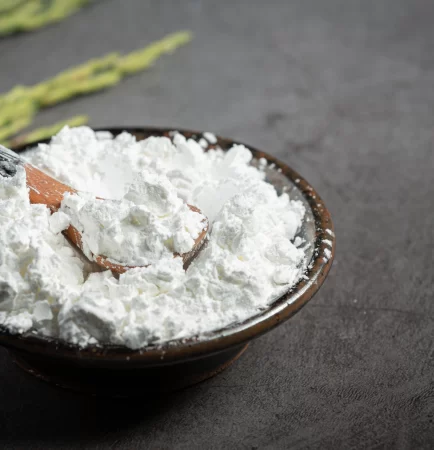 Fine calcined clay powder placed in a bowl with a wooden spoon on a dark surface