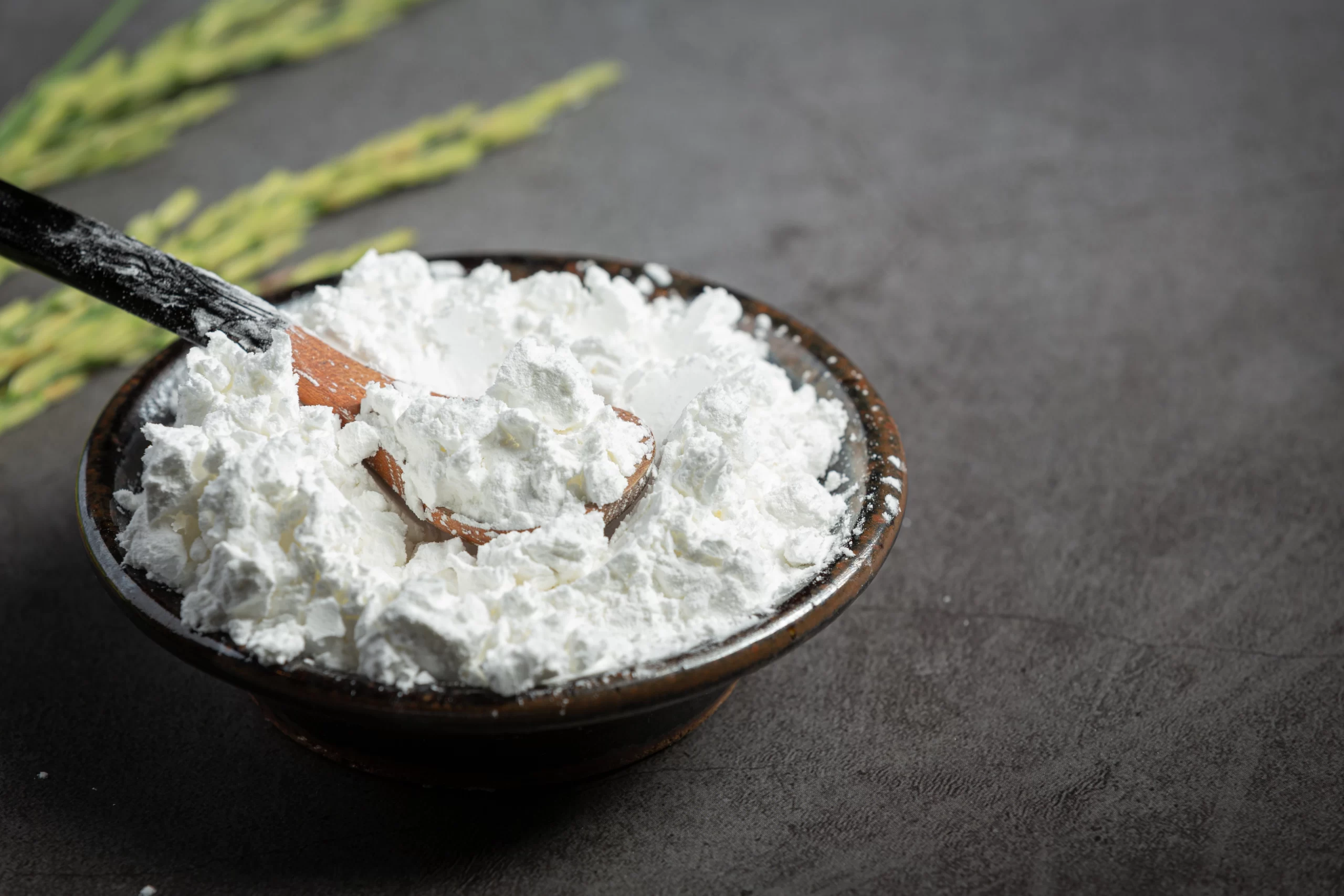 Fine calcined clay powder placed in a bowl with a wooden spoon on a dark surface
